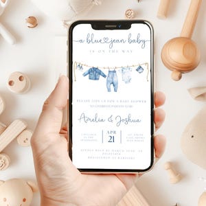 May include: A smartphone displays a baby shower invitation with the text "a blue jean baby is on the way." The invitation features watercolor illustrations of baby clothes hanging on a clothesline. The names Amelia & Joshua are also displayed.