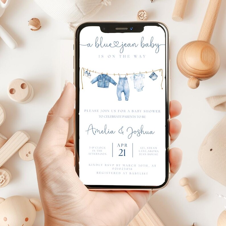 May include: A smartphone displays a baby shower invitation with the text "a blue jean baby is on the way." The invitation features watercolor illustrations of baby clothes hanging on a clothesline. The names Amelia & Joshua are also displayed.