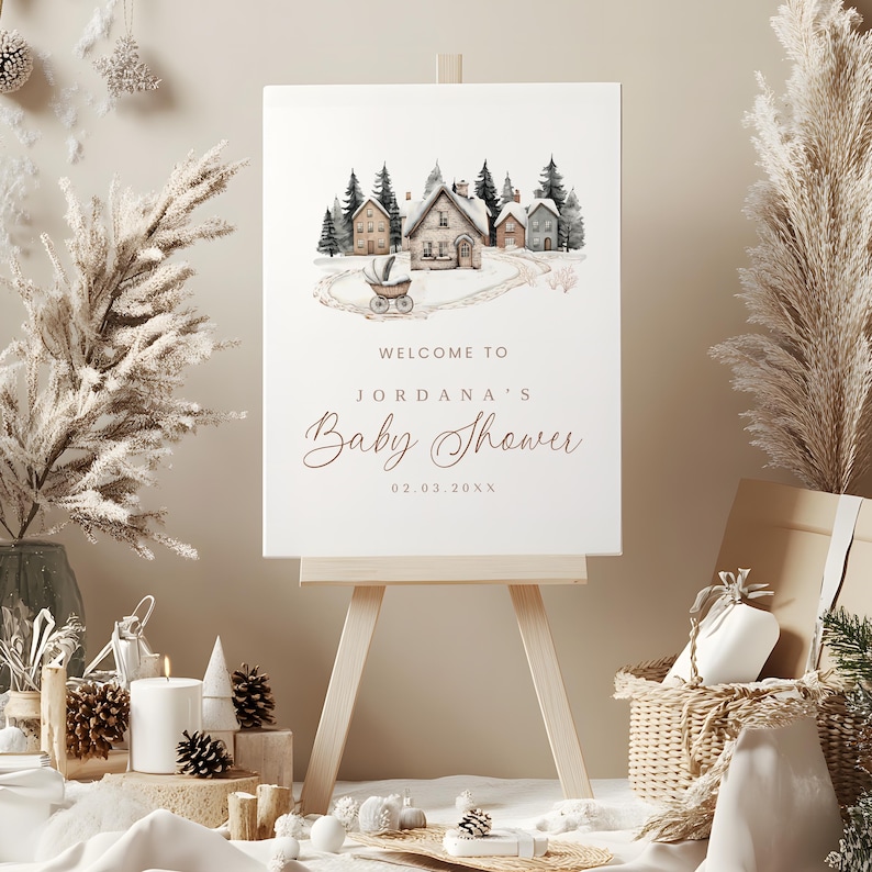 May include: A baby shower sign on a wooden easel. The sign features a watercolor illustration of a snowy village scene with a baby carriage. The text reads "Welcome to Jordana's Baby Shower" and the date.