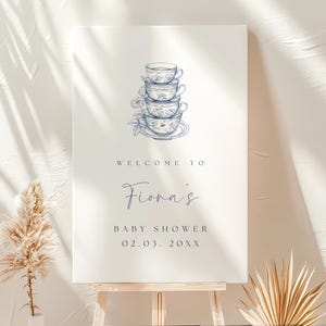 May include: A white welcome sign with blue text and a blue and white illustration of a stack of teacups. The text reads "Welcome to Fiona's Baby Shower 02.03.20XX".