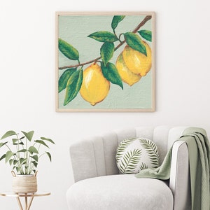 May include: A square framed wall art print featuring a painting of two bright yellow lemons hanging from a brown branch with several dark green leaves against a light sage green background, enclosed in a simple light-colored wooden frame.