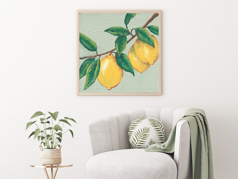 May include: A square framed wall art print featuring a painting of two bright yellow lemons hanging from a brown branch with several dark green leaves against a light sage green background, enclosed in a simple light-colored wooden frame.