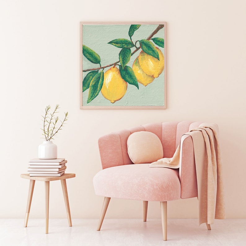 May include: A square framed painting featuring two bright yellow lemons hanging from a brown branch with dark green leaves against a pale mint green background. The artwork is displayed on a wall above a pink upholstered chair and a small wooden side table.
