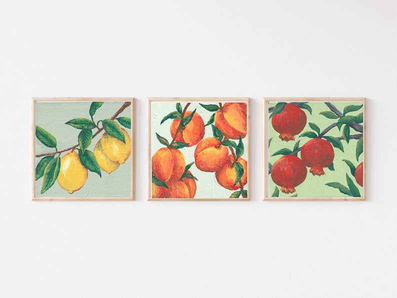 May include: A set of three square framed wall art prints. The first print shows yellow lemons on a branch with green leaves. The second print features orange peaches on a branch. The third print displays red pomegranates on a branch with green leaves.