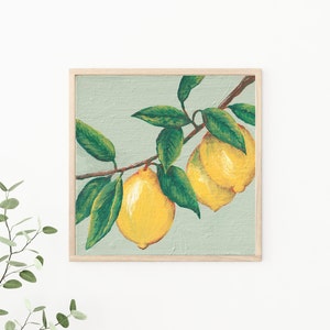 May include: A square wall art print in a light wood frame featuring an acrylic painting of two bright yellow lemons hanging from a brown branch with several dark green leaves against a textured pale sage green background.