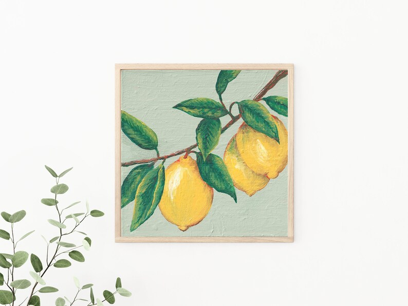 May include: A square wall art print in a light wood frame featuring an acrylic painting of two bright yellow lemons hanging from a brown branch with several dark green leaves against a textured pale sage green background.