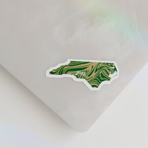 May include: A green and brown swirl sticker of the state of North Carolina with the word "49ers" written in white.