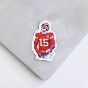 May include: A sticker featuring a football player wearing a red and white jersey with the number 15. The player is in a celebratory pose with his arms raised.