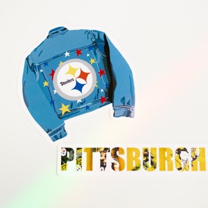 May include: A blue denim jacket with a Pittsburgh Steelers logo and yellow stars. The word "Pittsburgh" is written in yellow letters on a white background.