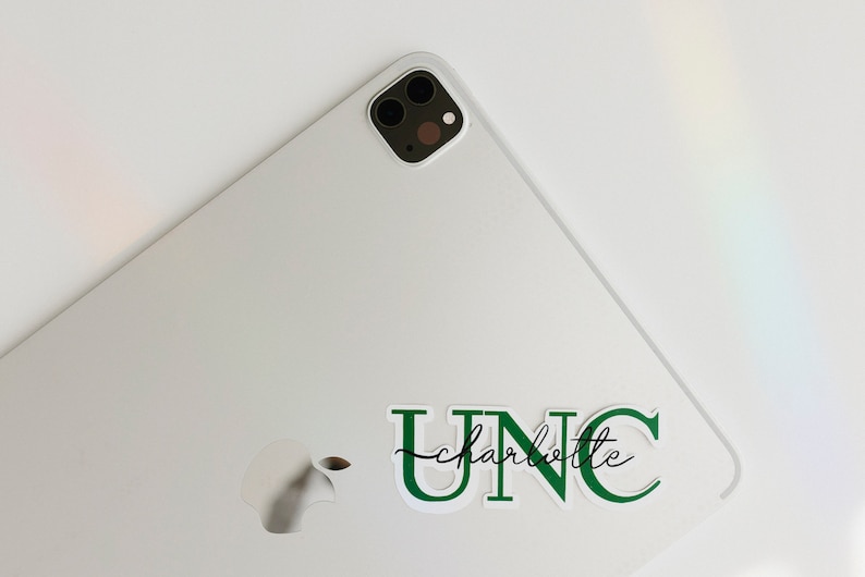 May include: A white laptop with a green UNC Charlotte sticker on the back. The laptop has a silver Apple logo on the back.