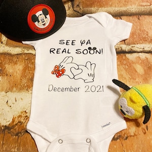 May include: White onesie with a Mickey Mouse and Minnie Mouse hand design. The onesie says "See ya real soon! December 2021".