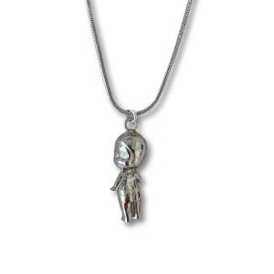 May include: A silver necklace with a pendant in the shape of a stylized figure. The pendant is attached to a fine chain. The figure has a rounded head and a slender body. The necklace is set against a white backdrop.