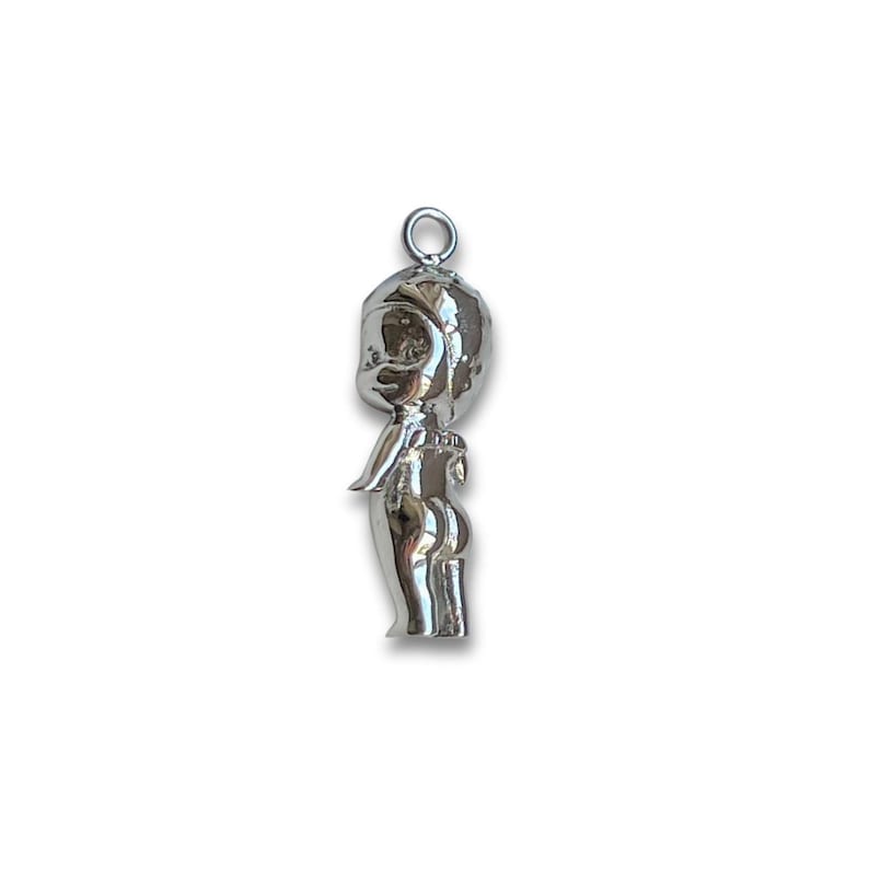 K&ouml;nnte beinhalten: Ein silberfarbener Anh&auml;nger in Form einer stilisierten Figur mit rundem Kopf, kleinen Armen und einem abgerundeten Unterteil. Der Anh&auml;nger hat oben eine Schlaufe zum Befestigen an einer Halskette oder einem Armband. Die Figur steht aufrecht.