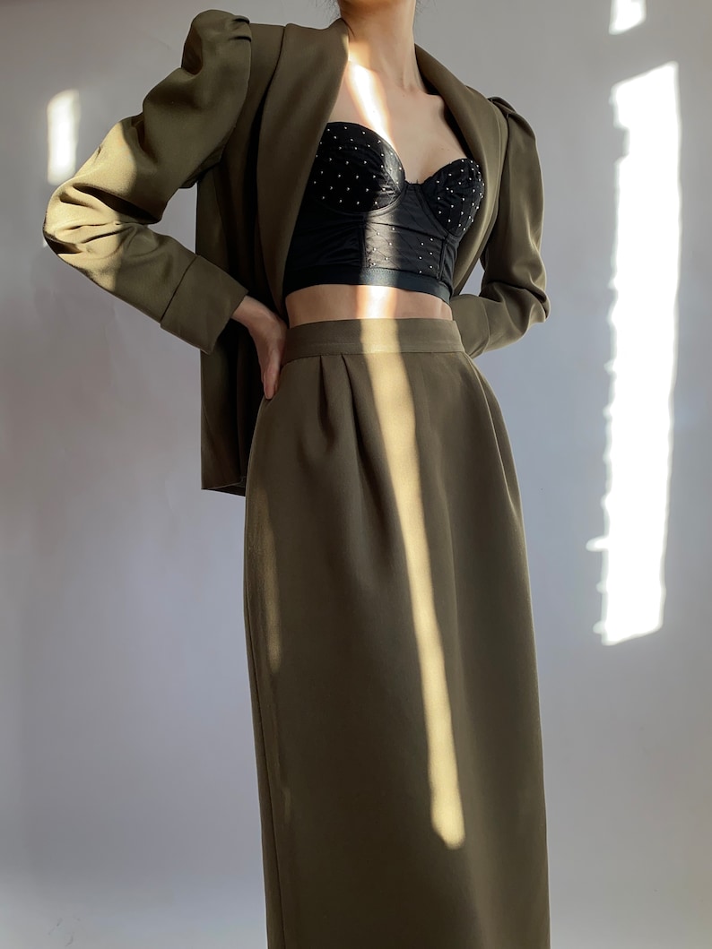 May include: A green blazer with puffed sleeves and a matching green skirt. The blazer is open and a black lace bra is visible underneath.