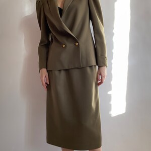 May include: A green double-breasted blazer with puffed shoulders and a matching skirt. The blazer has gold buttons.