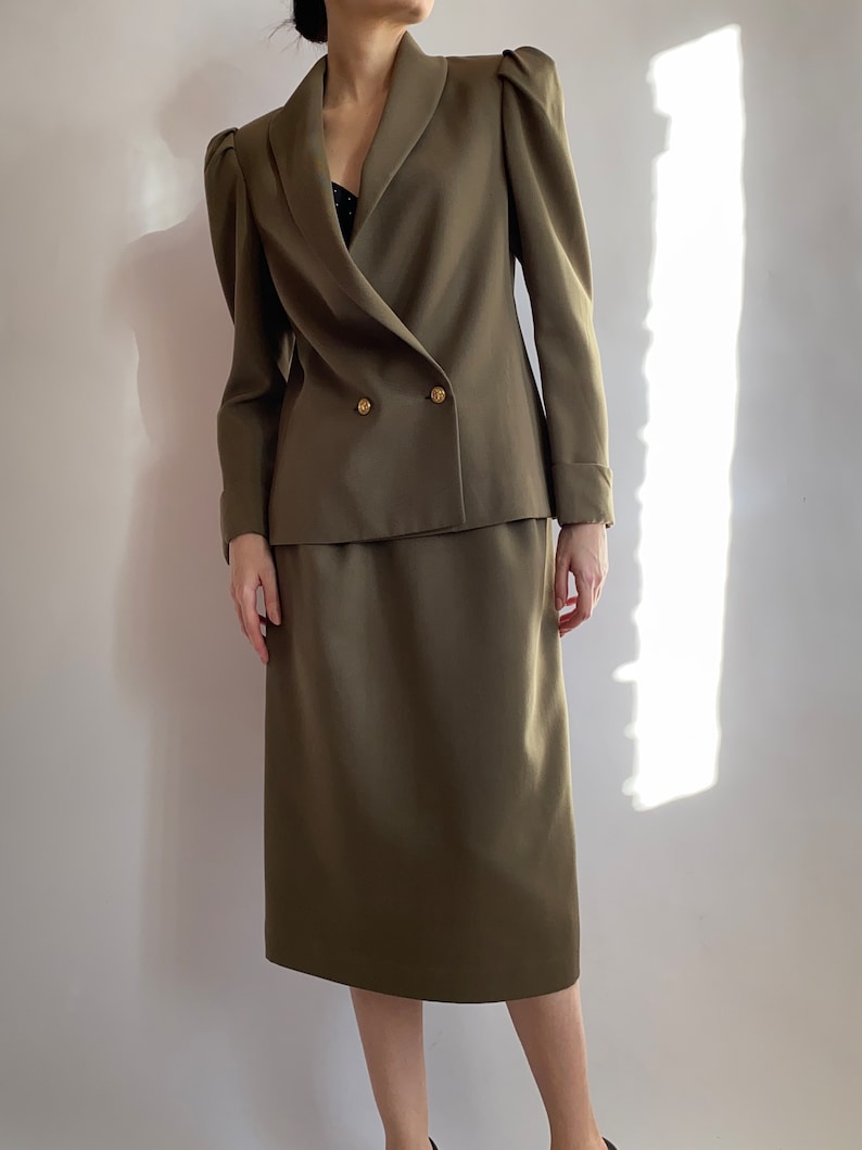 May include: A green double-breasted blazer with puffed shoulders and a matching skirt. The blazer has gold buttons.