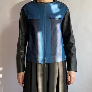 May include: A blue and black denim jacket with leather sleeves. The jacket has a zip fastening and two pockets on the front.