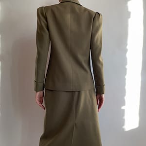 May include: A brown skirt suit with a blazer featuring puffed shoulders and a skirt that hits just above the knee.