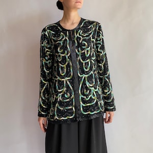 May include: A black sequined jacket with a green and blue abstract pattern. The jacket has a long sleeve and a button closure.