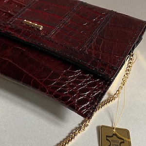 May include: A burgundy leather clutch purse with a gold chain strap and a small gold tag that reads "Echtes Leder".