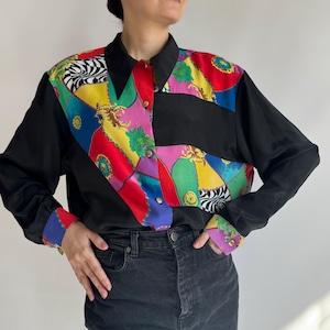 Puede incluir: Camisa negra de manga larga con un diseño de patchwork colorido en la parte delantera y los puños. El patchwork presenta patrones vibrantes en rojo, amarillo, verde y morado, con detalles de botones dorados. La camisa tiene un cuello clásico.