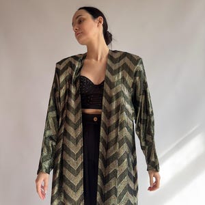 May include: A long-sleeved gold and black chevron patterned jacket. The jacket has a relaxed fit and a slightly open front.
