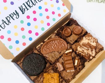 May include: A box of chocolate brownies with assorted toppings like an Oreo, chocolate bars, and a caramel biscuit. The lid features a polka dot design and the words "Happy Birthday".