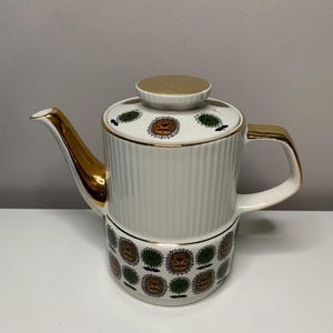 May include: White ceramic teapot with a gold trim and a green and gold floral pattern. The teapot has a lid with a gold knob.