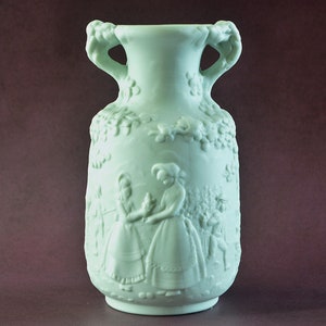 May include: A pale green ceramic vase with a raised design of people and flowers. The vase has two handles and a rounded body.