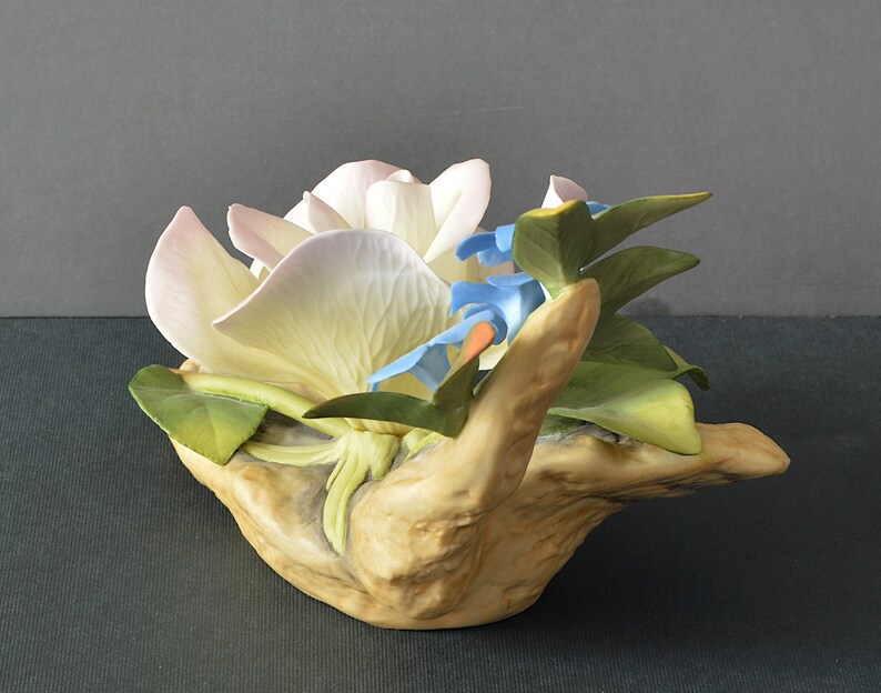 May include: A porcelain figurine of a white and pink flower with blue flowers nestled in a sculpted wooden base.