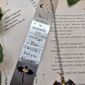 May include: A silver metal bookmark with a chain and charm. The bookmark has etched text: "There's nowhere in existence you could go. That I wouldn't find you, Violence." A black and yellow dragon is at the bottom.