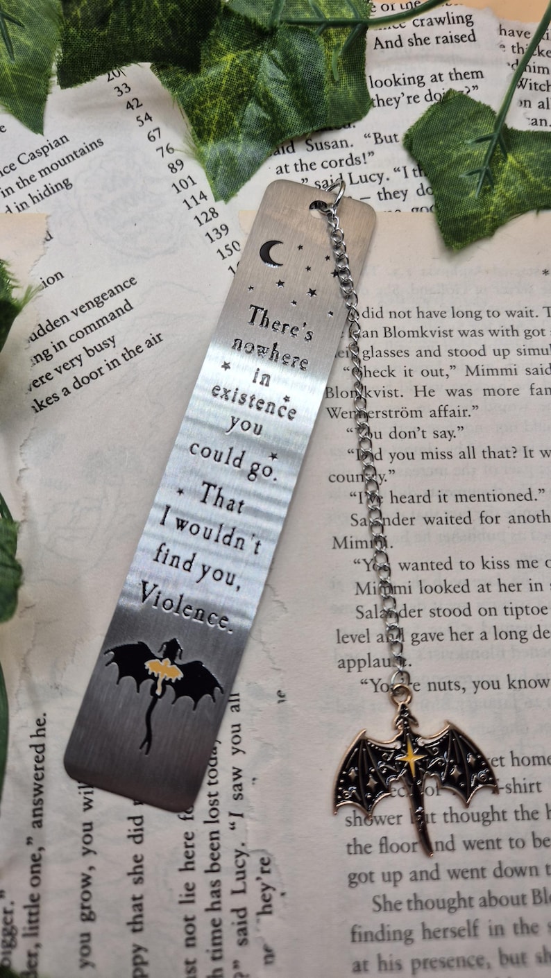 May include: A silver metal bookmark with a chain and charm. The bookmark has etched text: "There's nowhere in existence you could go. That I wouldn't find you, Violence." A black and yellow dragon is at the bottom.