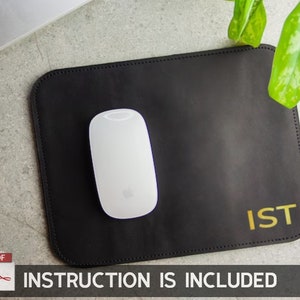 May include: Black leather mouse pad with gold lettering that says "IST". A white wireless mouse is on the pad.
