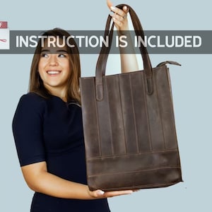 Puede incluir: Una mujer sostiene una bolsa de mano de cuero marrón con cierre de cremallera. La bolsa tiene un diseño estructurado con costuras verticales. El texto "INSTRUCTION IS INCLUDED" se muestra sobre la bolsa.