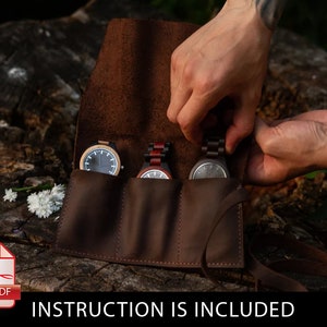 May include: A brown leather watch roll with three slots for watches. The roll is open and three watches are visible. The watches have wooden cases and different colored bands.