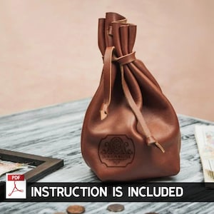 Puede incluir: Una bolsa de dados de cuero marrón con cierre de cordón. La bolsa tiene un logotipo en relieve que dice "Dungeon Master".