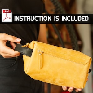 Può includere: Un beauty case in pelle gialla con una cerniera nera e un manico in pelle nera. La borsa è tenuta da una persona. Il testo "INSTRUCTION IS INCLUDED" è visibile nell'immagine.
