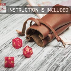 May include: A brown leather dice bag with a drawstring closure. The bag is lying on a wooden surface with three red dice, one with the number 5, one with the number 10, and one with the number 15.