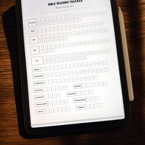 May include: A black tablet displaying a "BIBLE READING TRACKER" for the New Testament. The tracker lists books of the Bible with checkboxes for each chapter. A white stylus rests on the right side of the tablet, on a dark wooden surface.
