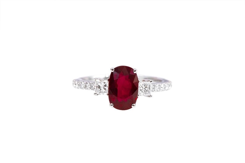 K&ouml;nnte beinhalten: Ein silberner Ring mit einem gro&szlig;en ovalen Rubin, der von kleineren Diamanten umgeben ist.