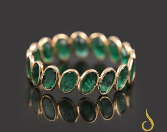 May include: A gold band ring with a row of oval-shaped emerald green gemstones.