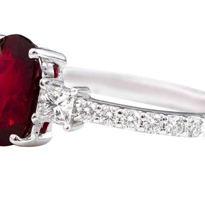 K&ouml;nnte beinhalten: Ein silberner Ring mit einem gro&szlig;en ovalen Rubin-Edelstein und kleineren Diamant-Akzenten auf der Ringschiene.