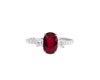 May include: A silver ring featuring a large oval ruby gemstone surrounded by smaller diamonds.