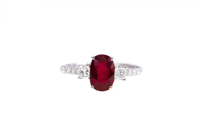K&ouml;nnte beinhalten: Ein silberner Ring mit einem gro&szlig;en ovalen Rubin, der von kleineren Diamanten umgeben ist.