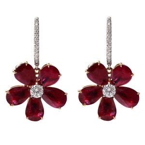 Puede incluir: Un par de pendientes con forma de flor. Cada pendiente presenta cinco pétalos de rubí rojo oscuro que rodean una piedra preciosa central, redonda y transparente. Los pendientes están suspendidos de un aro con diamantes.