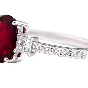 K&ouml;nnte beinhalten: Ein silberner Ring mit einem gro&szlig;en ovalen Rubin-Edelstein und kleineren Diamant-Akzenten auf der Ringschiene.