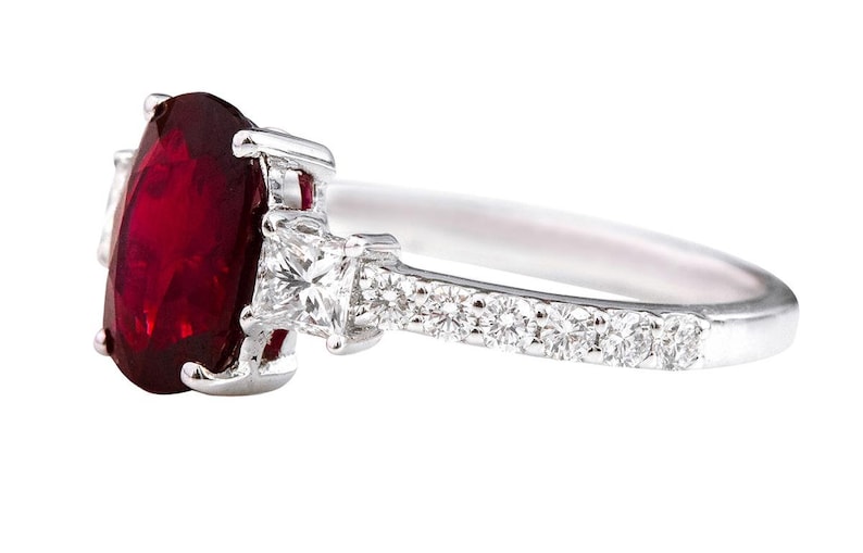 K&ouml;nnte beinhalten: Ein silberner Ring mit einem gro&szlig;en ovalen Rubin-Edelstein und kleineren Diamant-Akzenten auf der Ringschiene.
