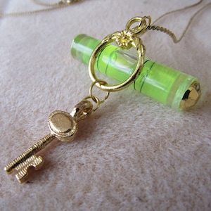 May include: A gold necklace with a green glass level pendant and a gold key charm.