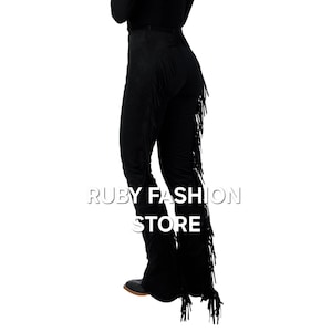 May include: Black suede pants with fringe detail on the sides. The pants are fitted through the hips and legs and have a wide leg opening. The fringe is long and flowing, and the pants are a stylish and unique piece of clothing.