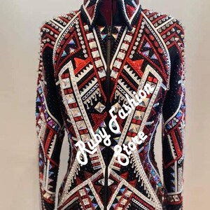 May include: A black jacket with a front zipper, featuring intricate red and white geometric patterns, silver studs, and numerous clear and red crystals. The text 'Red on Black Base' and 'Ruby Fashion Store' is overlaid on the image.